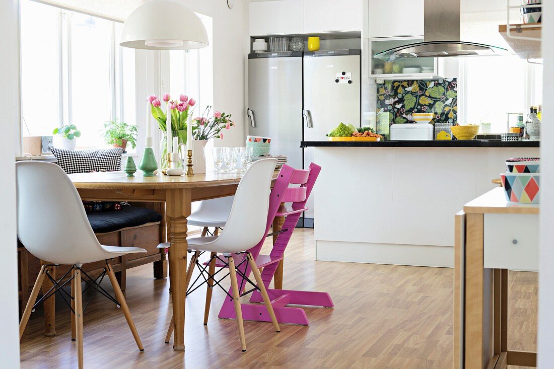 Holztisch mit Klassiker Schalenstühlen und pinkfarbenem Tripp Trapp, im Hintergrund Theke in offener Küche
