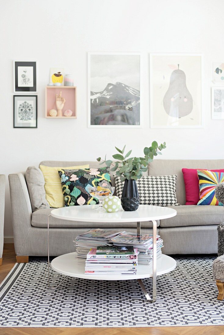 Runder Beistelltisch vor grauem Sofa, auf Teppich mit Retro Muster, gerahmte Bilder an Wand