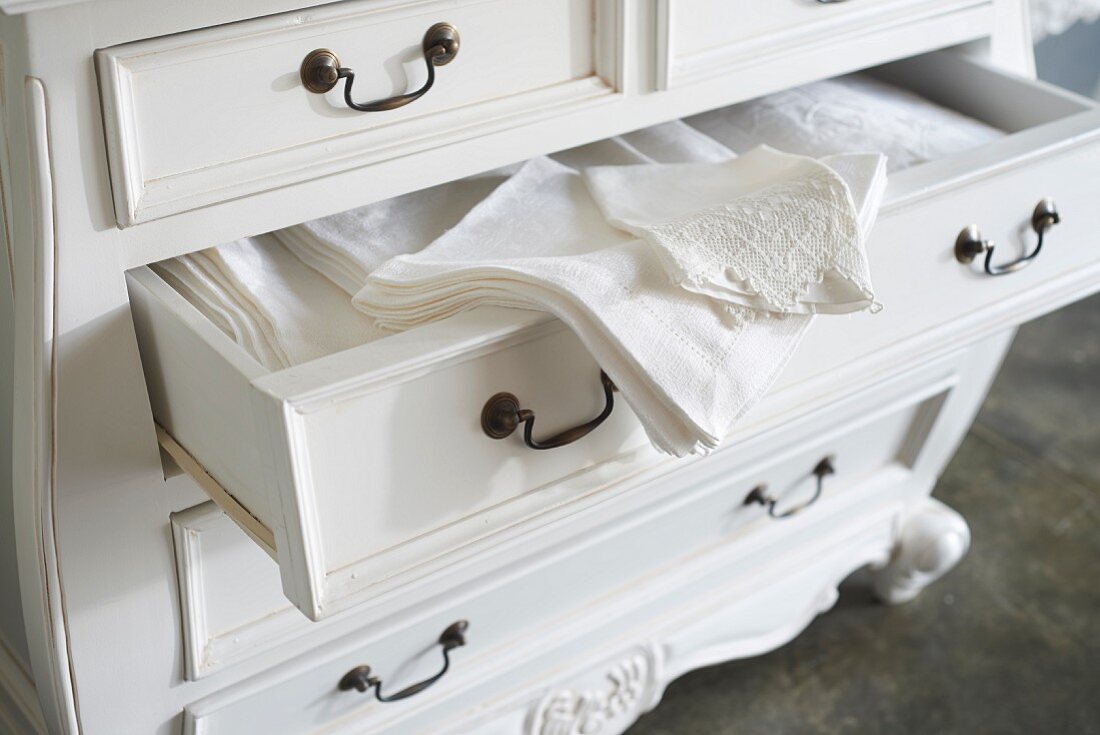 Elegant table linen in open drawer of white Baroque chest of drawers