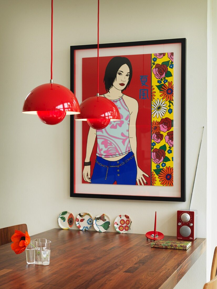 Red pendant lamp above walnut table below framed picture on wall