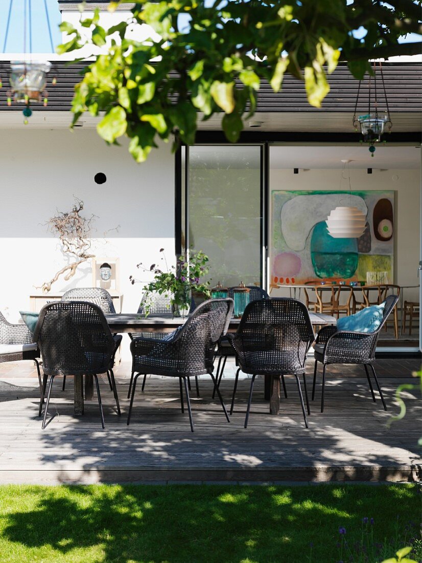 Grey-brown cane chairs around table on wooden terrace outside contemporary house