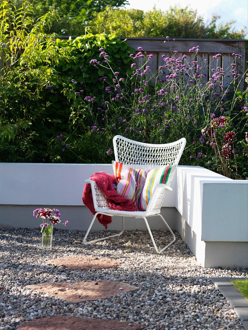 White wicker armchair and striped cushion on gravel terrace surrounded by low white wall