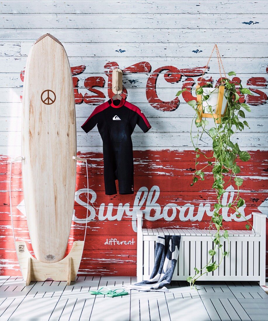 Maritime wall decoration - wetsuit hung from hook, surfboard and white wooden bench
