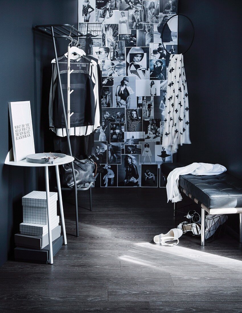 Offene Ankleideecke mit Wandtisch neben Garderobenständer aus Metall mit Kleidung, an schwarzer Wand peppige Schwarz-Weiß Fotos