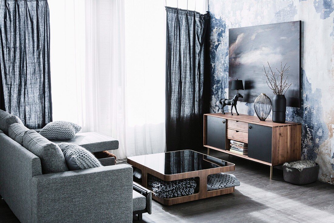 Graumeliert bezogene Couch und Tisch aus Walnussholz mit Ablagefächer, an Wand Sideboard