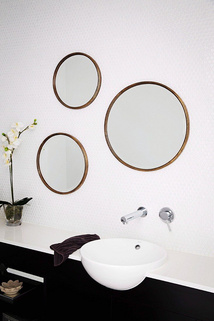 Aus alten, runden Bilderrahmen selbstgefertigtes Spiegeltrio über modernem Waschbecken mit Wandarmatur auf weissen Mosaikfliesen