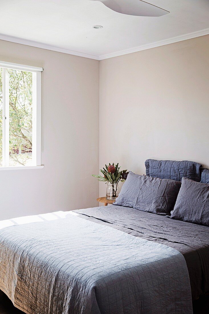 Schlichtes reduziertes Schlafzimmer mit beigefarbenen Wänden und violetter Bettwäsche