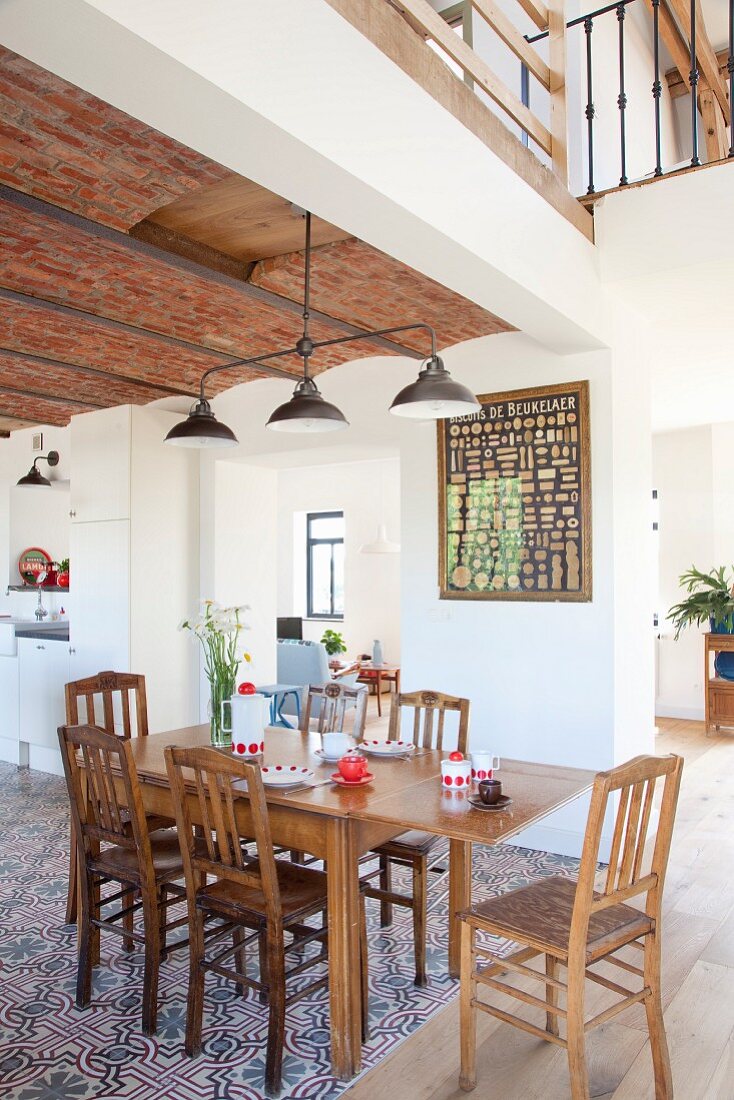 Dining area in open-plan interior with vintage metal pendant lamps hanging from ribbed brick ceiling