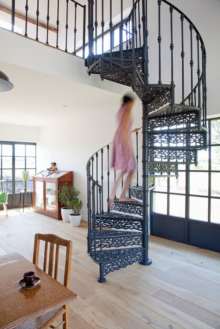 Woman walking up cast-iron spiral staircase in open-plan interior