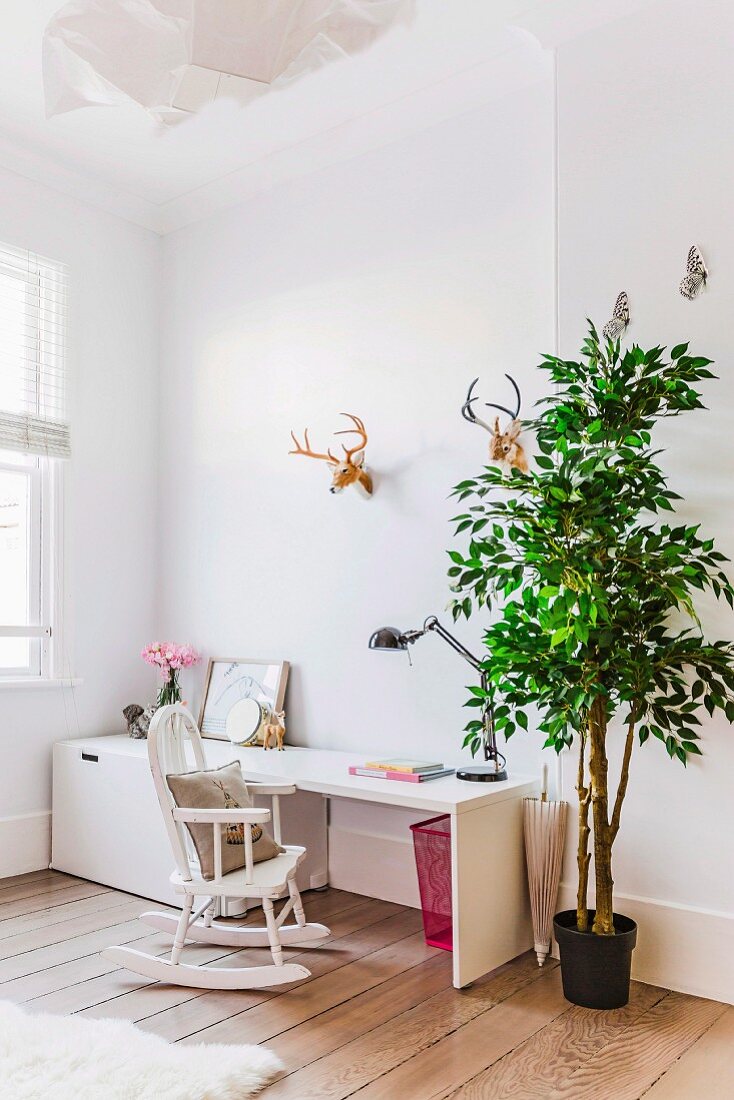 White desk, vintage rocking chair, green tree and faux hunting trophies in bright child's bedroom