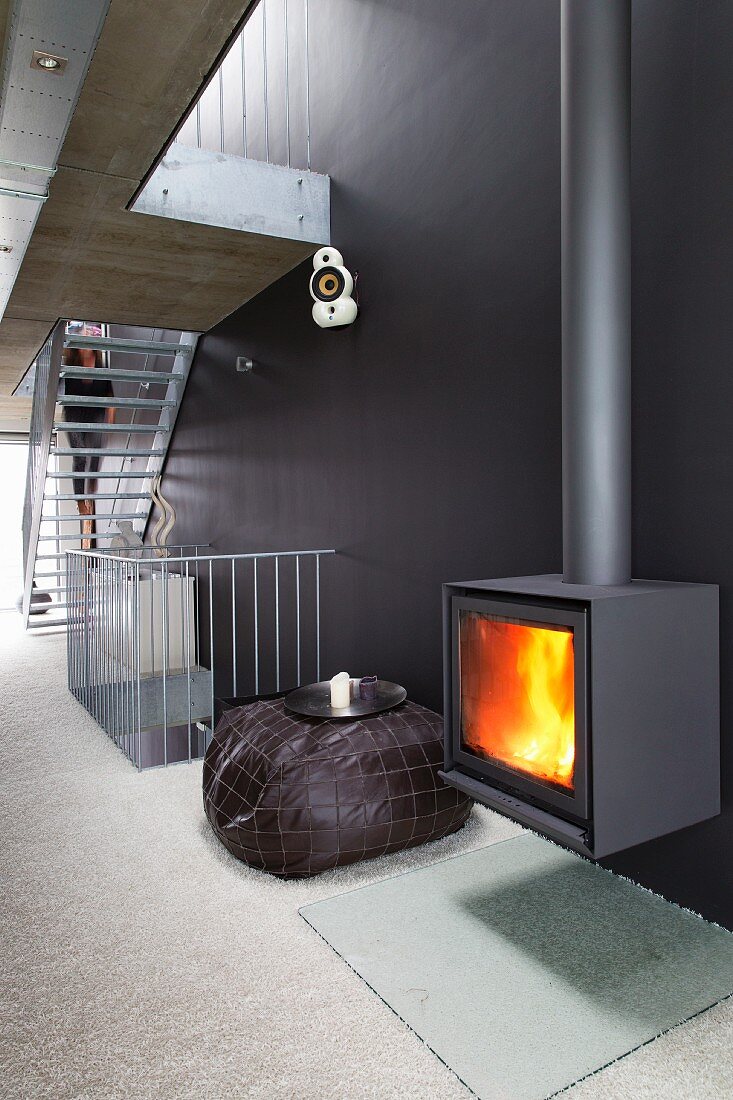 Fire in cast iron log burner on black wall in contemporary stairwell with staircase in background