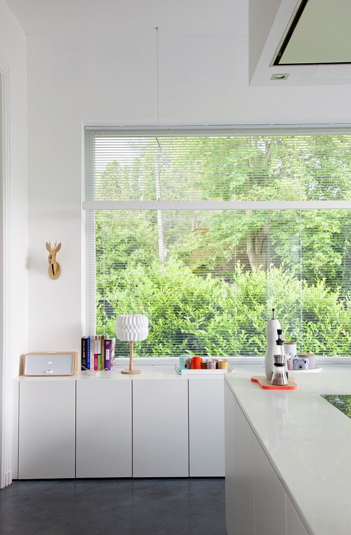weiße Küchenunterschränke vor Fenster mit Gartenblick