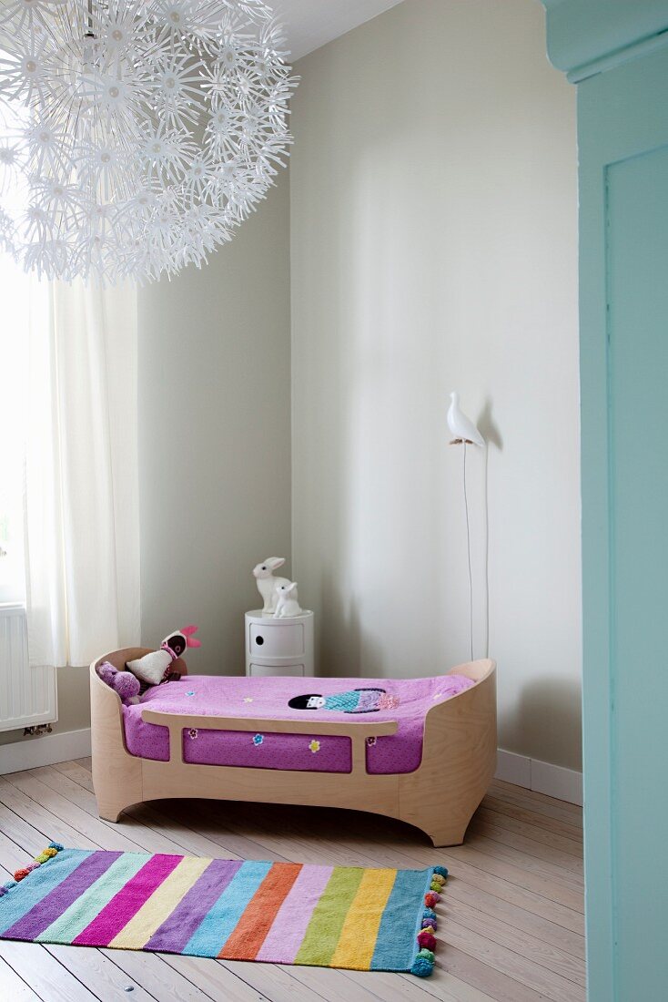 Striped rug next to designer child's bed on restored wooden floor below floral ceiling lamp