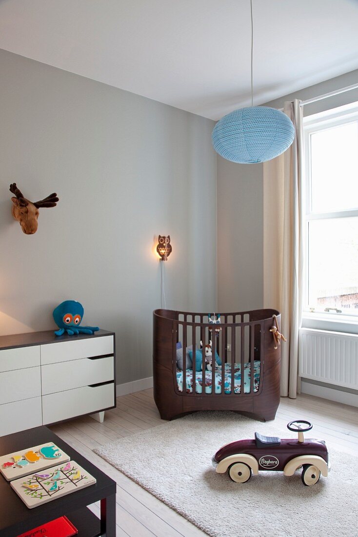 White retro chest of drawers, dark brown modern cot and ride-on toy car in nursery