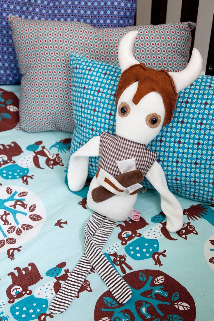 Fantasy figure soft toy on blue and brown, patterned bed linen and retro-patterned pillows in cot