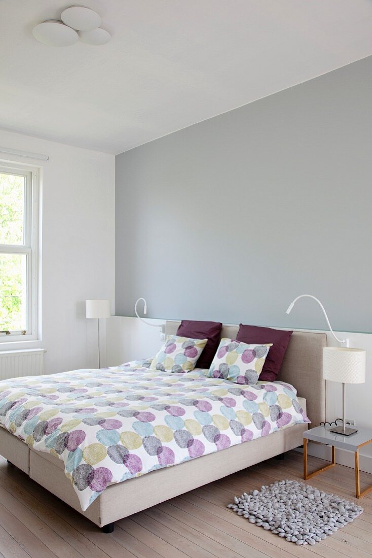 Double bed with pastel bed linen, grey-painted wall above white base element in minimalist bedroom