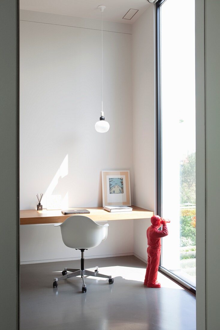 Floating wooden desk and retro swivel chair with shell seat next to floor-to-ceiling window