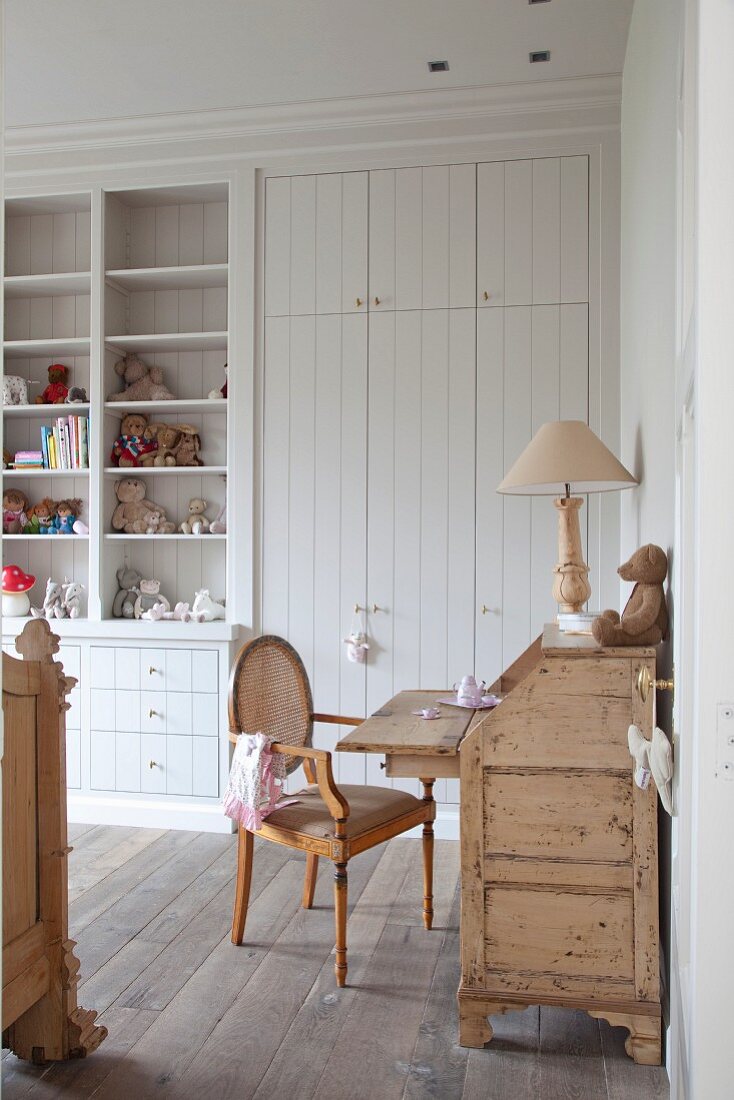Rococo-style chair at rustic wooden bureau in front of fitted wardrobe with white-painted doors in child's bedroom