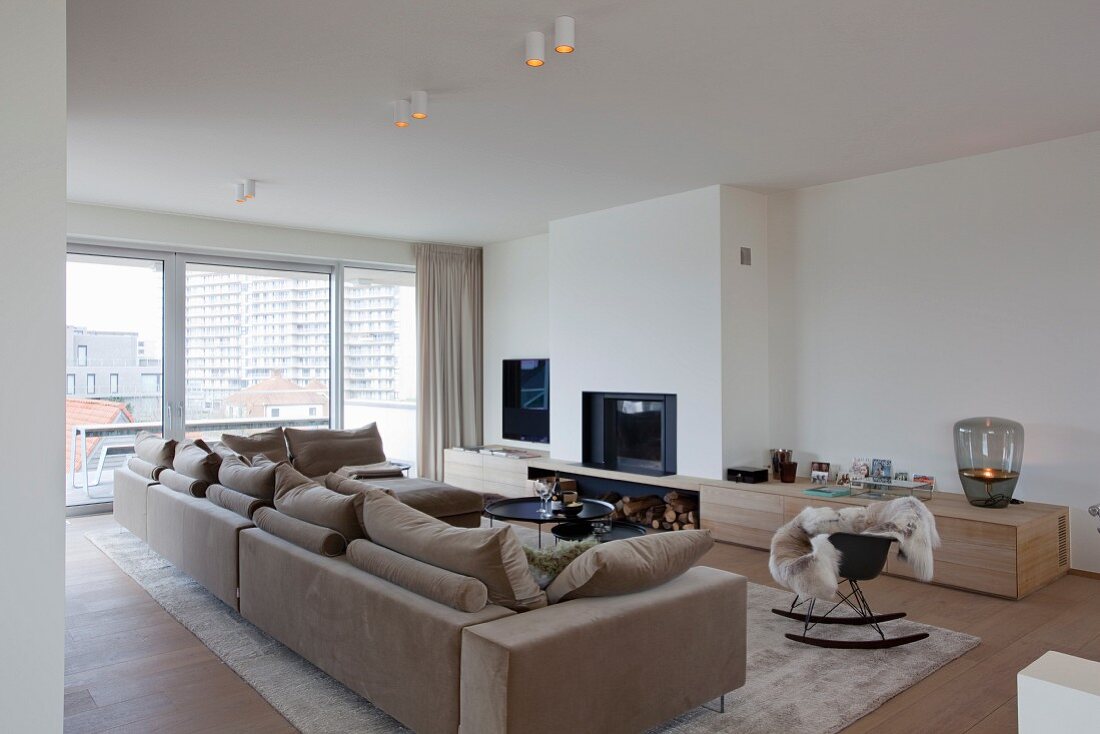 Elegant, minimalist urban apartment with beige sofa combination, open fireplace and low custom sideboard