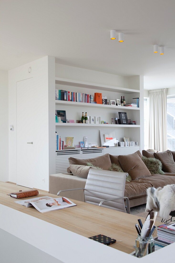Gemütliche Loungeecke mit beigefarbenem Polstersofa, weißer Regalwand und integriertem Schreibplatz