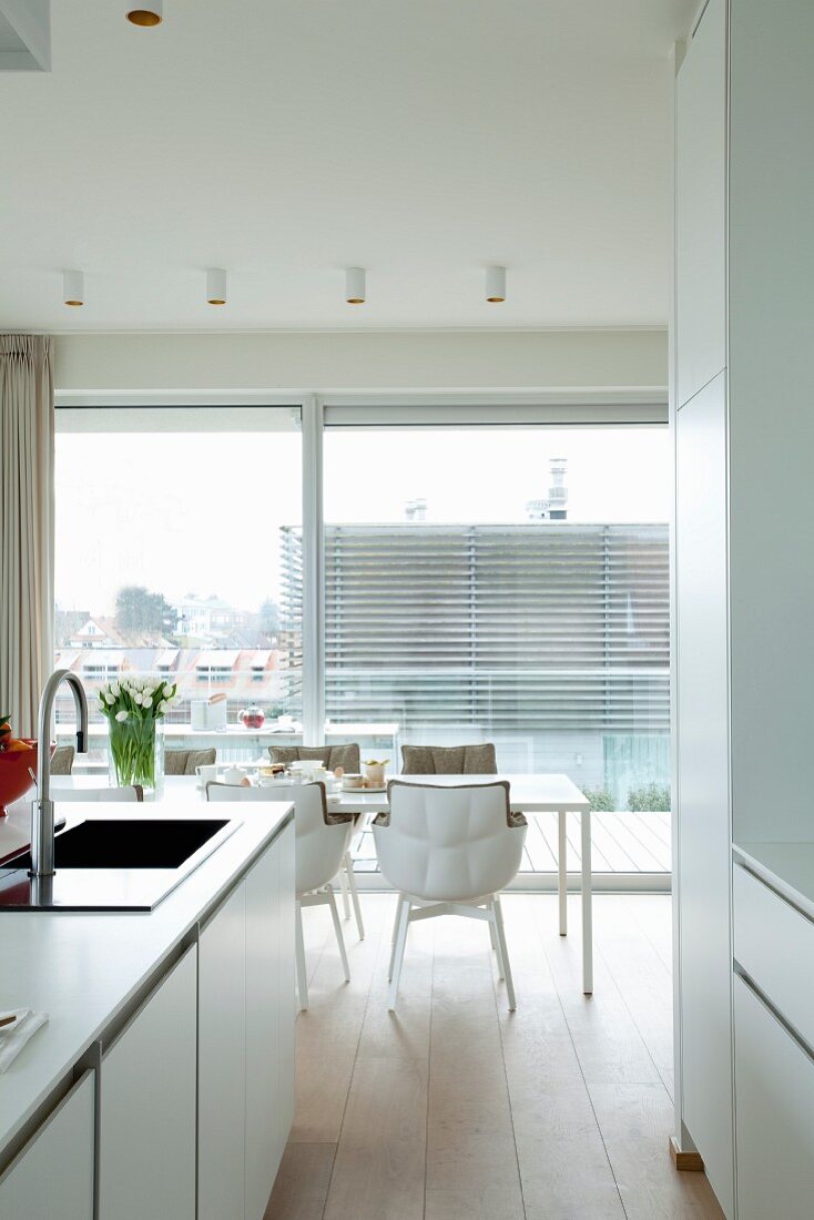 Blick von offener Küche auf hellen Esstisch mit Designerstühlen vor Fensterfront