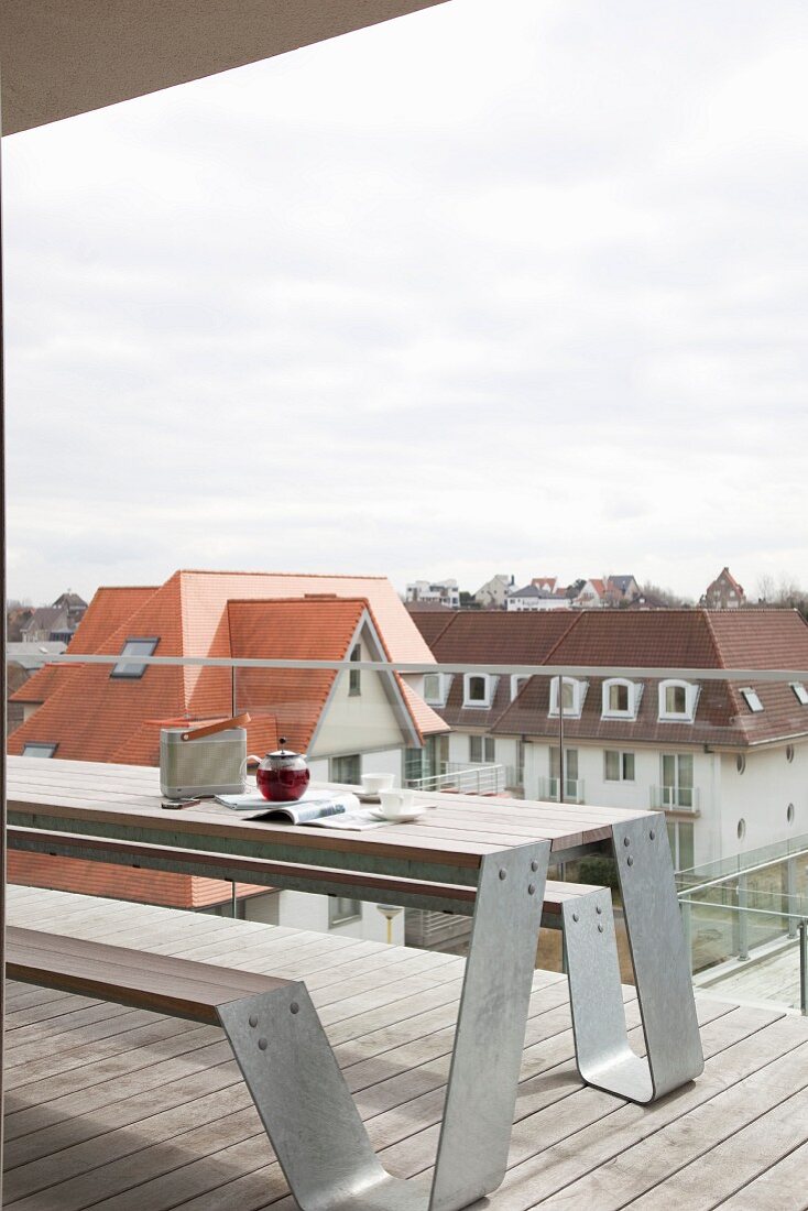 Modern wooden terrace with glass balustrade, bench and table combination and view of neighbouring buildings