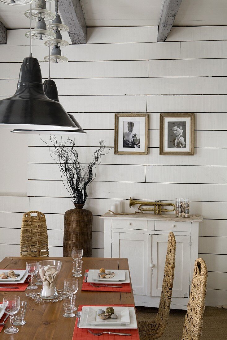 Set dining table below pendant lamps with black lampshades in white, wood-clad interior