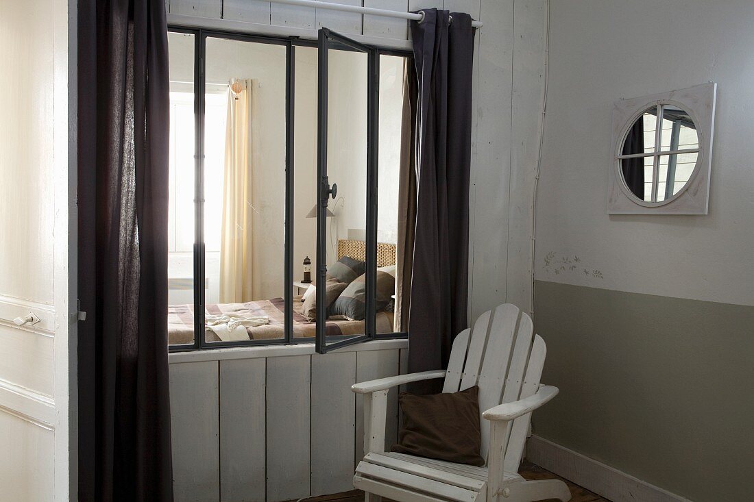 Armlehnstuhl aus weiss lackiertem Holz in Zimmerecke, neben Wand mit Fenstereinbau, Blick ins Schlafzimmer