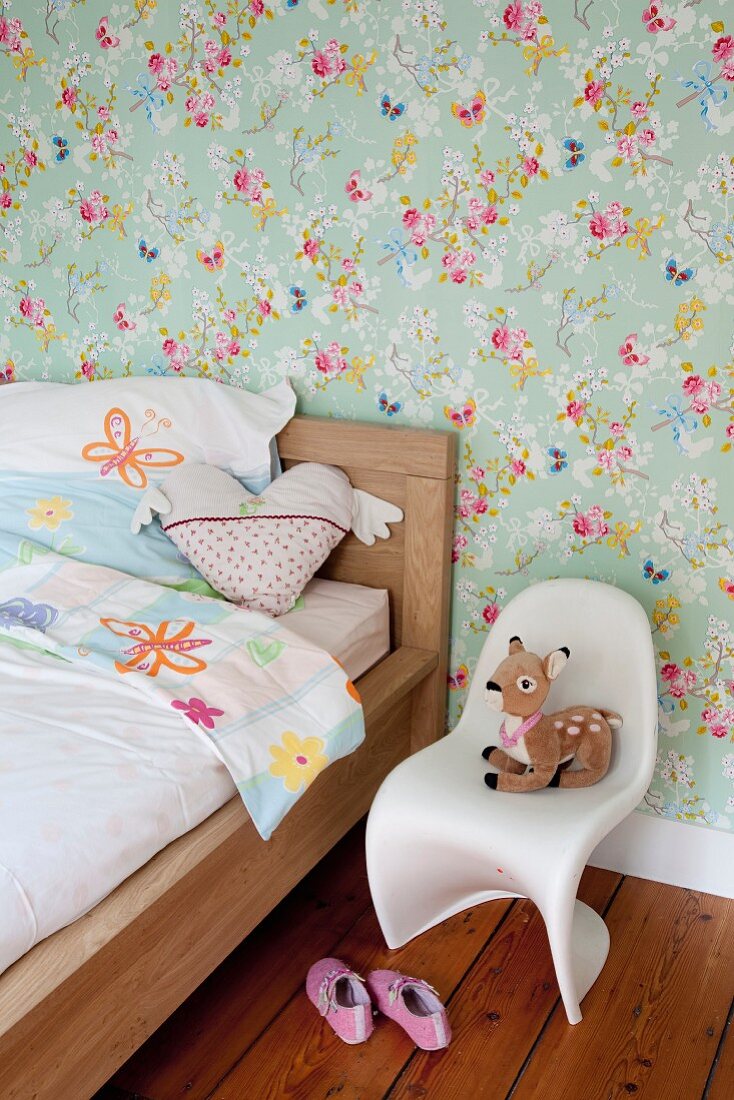 Wooden child's bed and soft toy on child's Panton chair against floral wallpaper