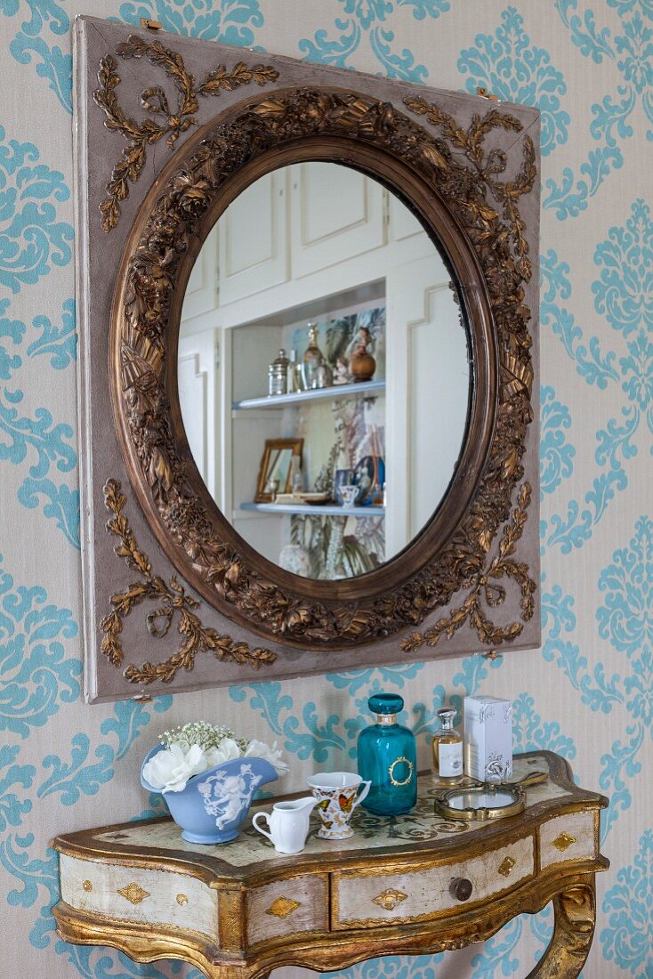 Antique mirror above gilt console table on ornate wallpaper