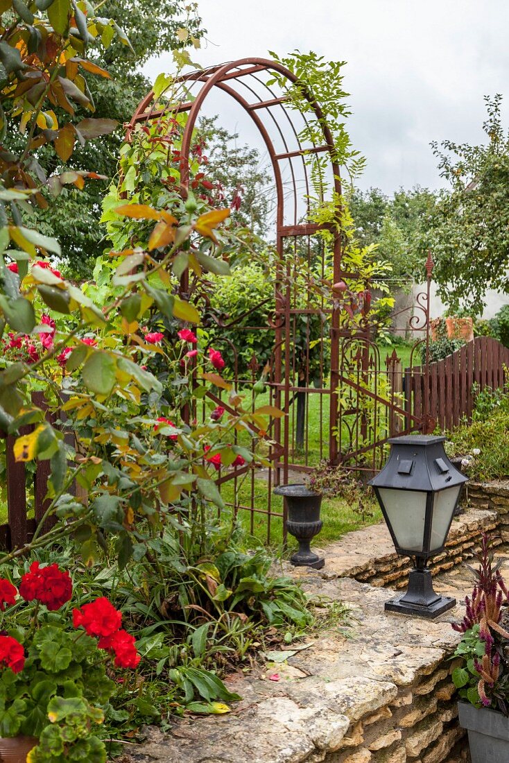 Metal trellis arch in summery, rustic garden with stone wall