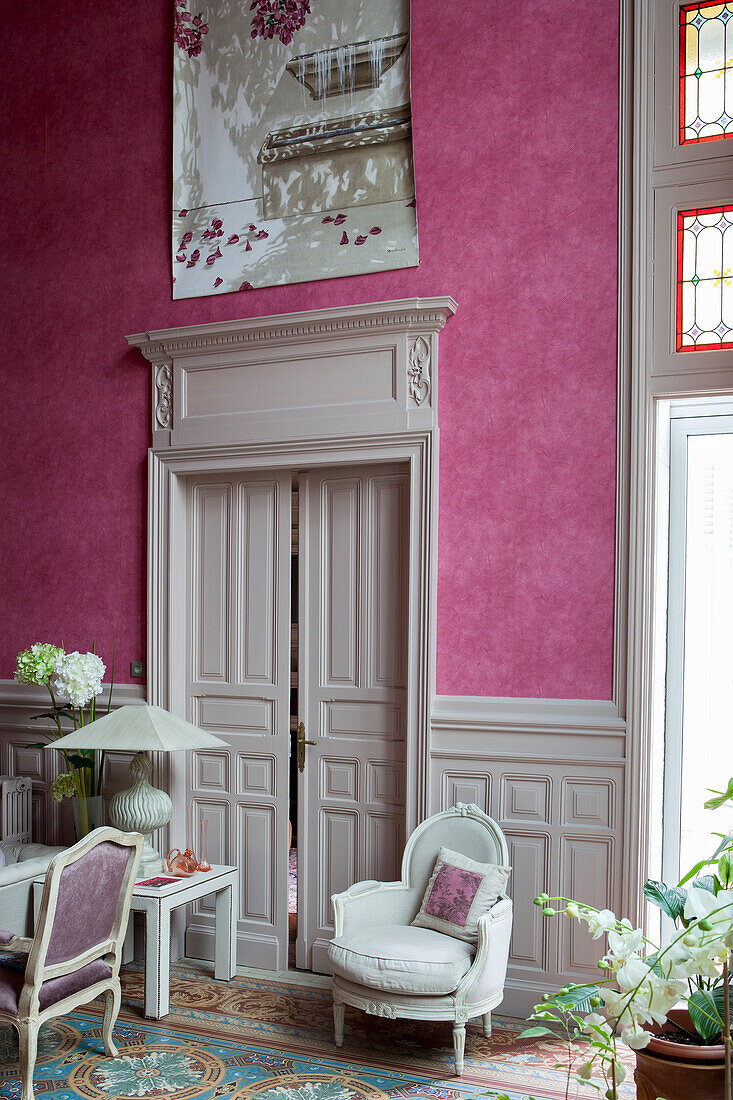 Pink wallpapered wall and white-painted double doors with carved frame behind Rococo armchair