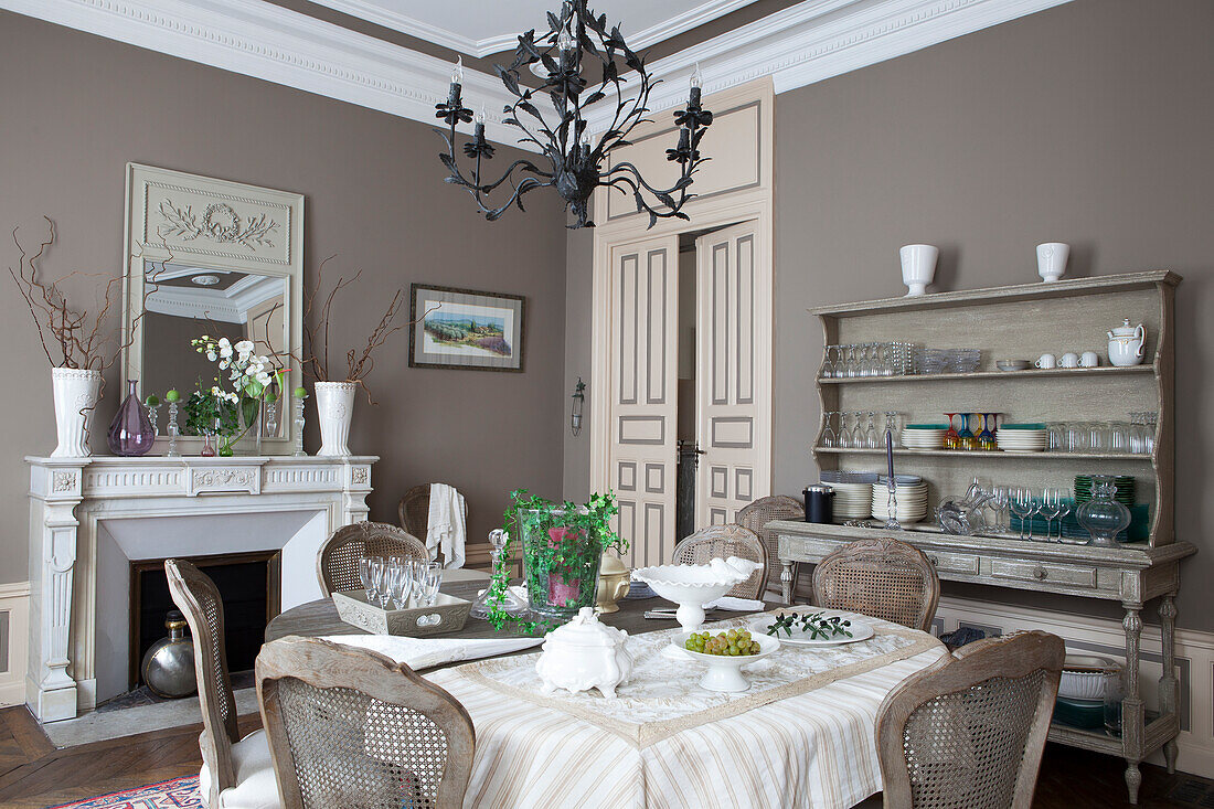 Chairs with curved backrests around table in front of dresser against wall in grand dining room with fireplace