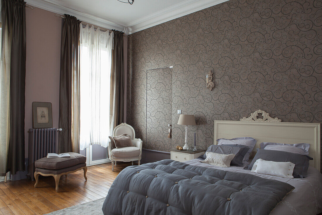 Grey quilt on elegant double bed with white-painted headboard against patterned wallpaper