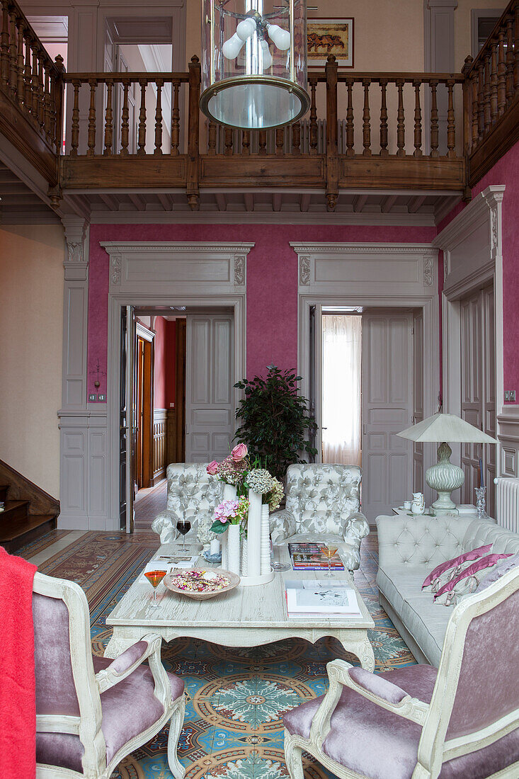 Antique chairs and couch around coffee table in grand, high-ceilinged foyer with encircling gallery