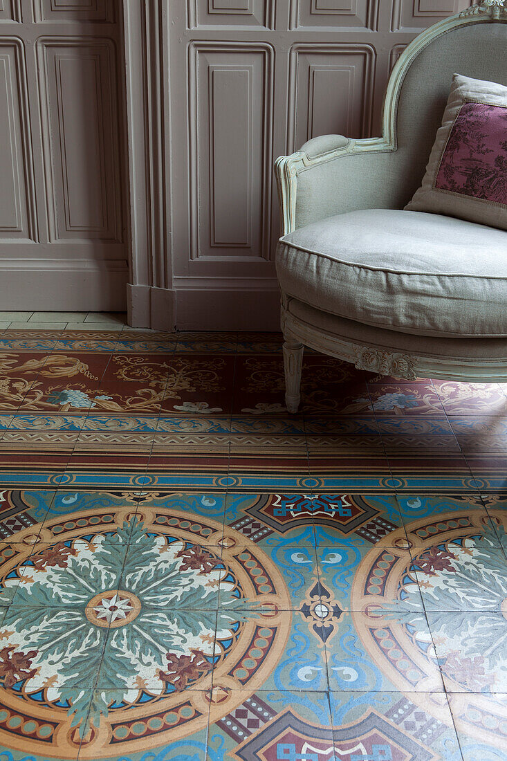 Elaborate, ornamental tiled floor, antique armchair and elegant pale grey wood panelling