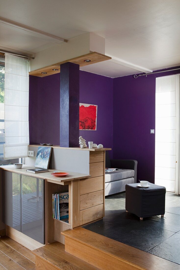 Counter with base cabinets adjoining platform in open-plan interior with purple-painted wall