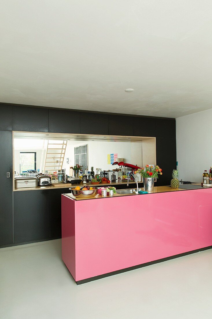 Kücheninsel mit pinkfarbener Front, im Hintergrund schwarzer Einbauschrank mit verspiegelter Wand in Nische