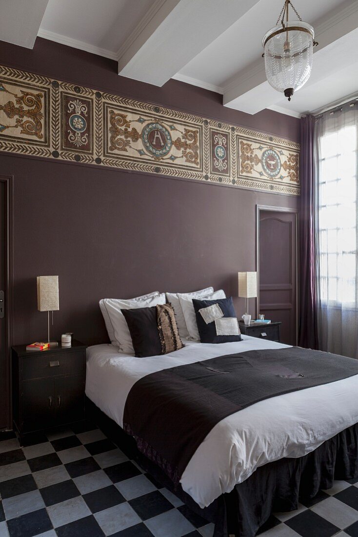 Doppelbett im Schlafzimmer mit Schachbrettmusterboden, an violett getönter Wand farbiges Fries im Jugendstil
