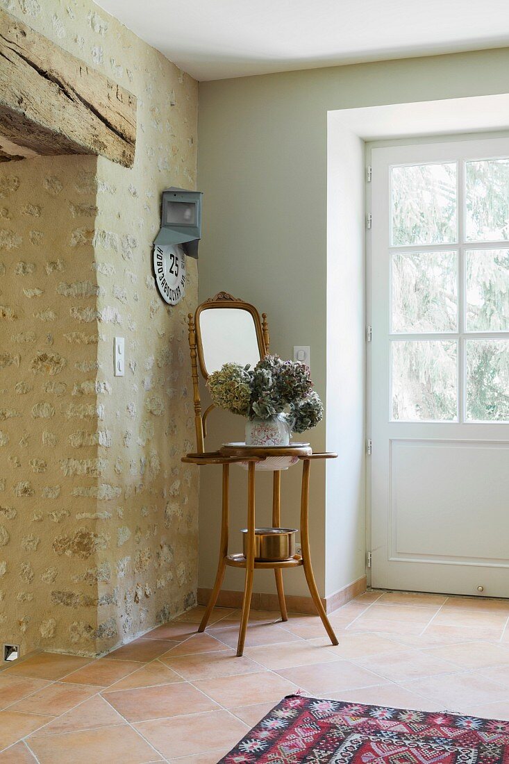 Foyer with stone wall, lattice front door and hydrangea and mirror on plant stand in corner
