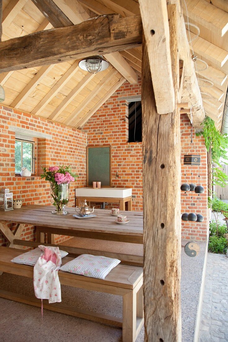 Roofed, rustic terrace in renovated farm building with exposed brickwork