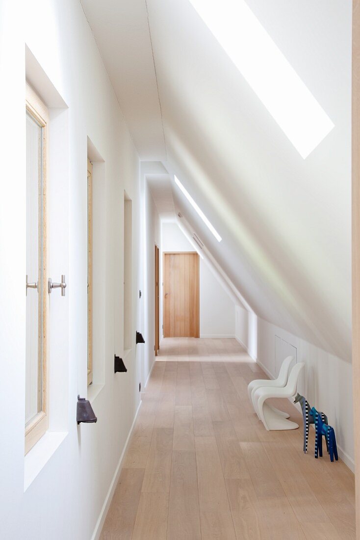 Corridor with wooden floor and children's white Panton chairs below sloping ceiling