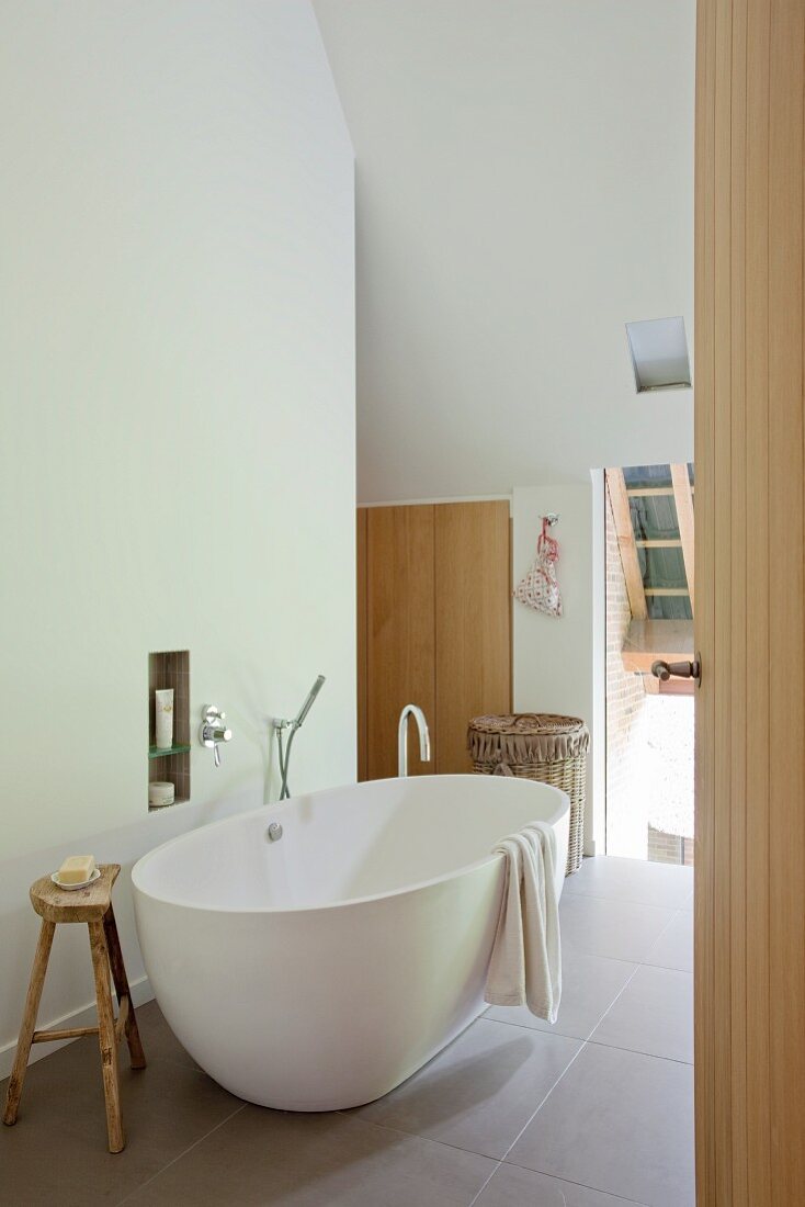 Free-standing white bathtub on large floor tiles in modern attic bathroom