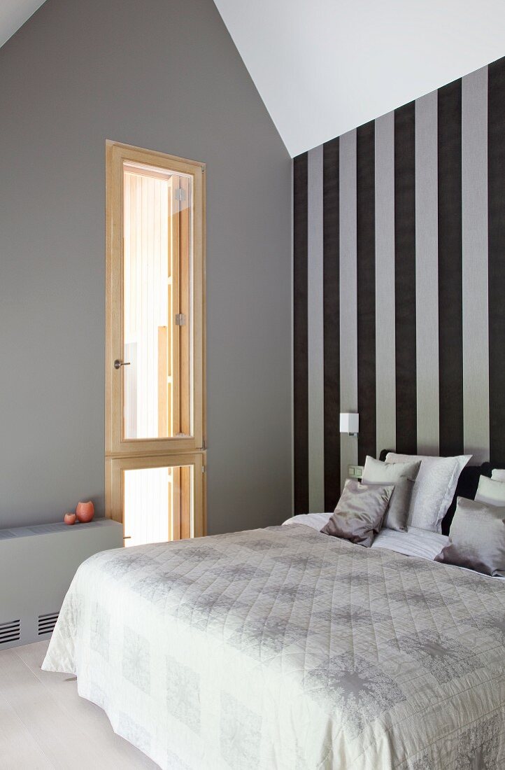 Doppelbett vor grau-schwarzer Streifentapete in minimalitstischem Dachgeschossschlafzimmer