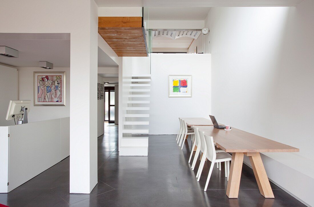 White chairs at wooden table in modern interior; minimalist staircase and gallery in background