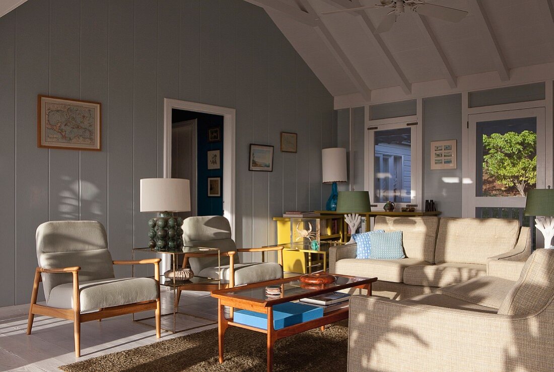 Sitzbereich mit 50er Jahre Retromöbeln im sonnigen Wohnraum eines grau-weiss gestrichenen Holzhauses
