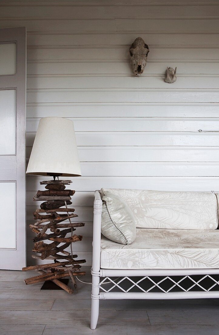 Maritime-style lamp base made of crossed pieces of driftwood next to ornate bamboo bench on white wooden veranda