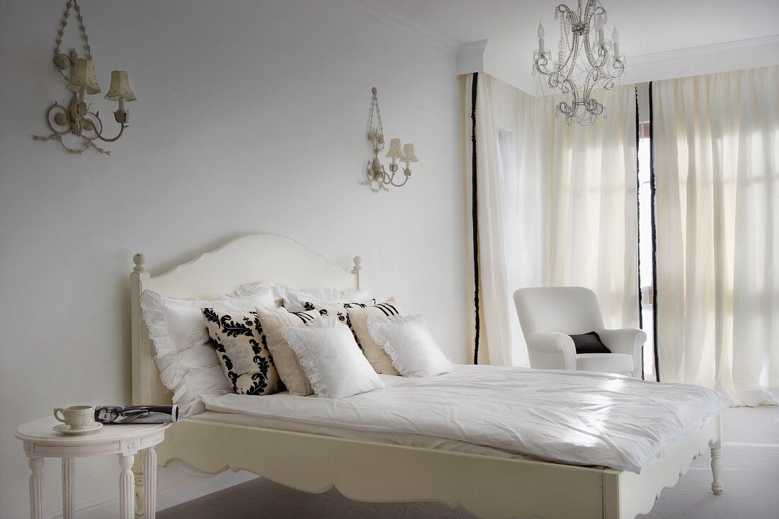 Weisses, elegantes Schlafzimmer mit Stilmöbeln, verzierten Wandlampen und Kronleuchter