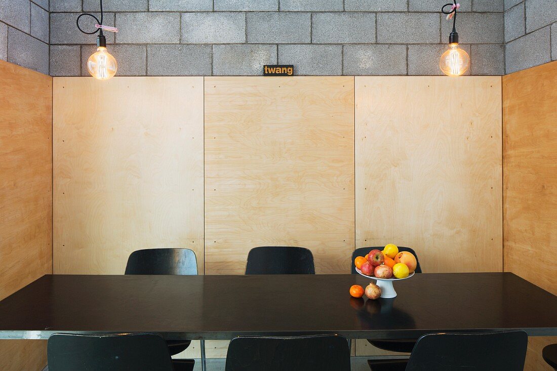 Fruit dish on black dining table in niche with wooden wall panels on concrete block walls