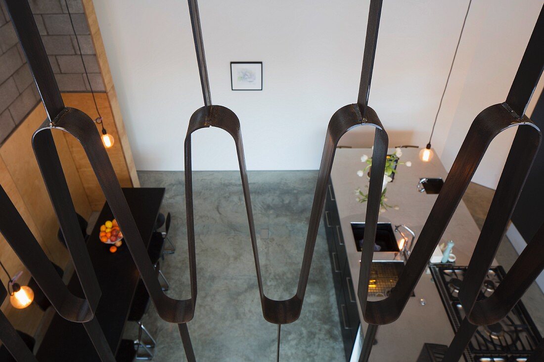 Blick durch Metallgeländer von Galerie in offenen Wohnraum mit Küchenblock aus Edelstahl und Essplatz